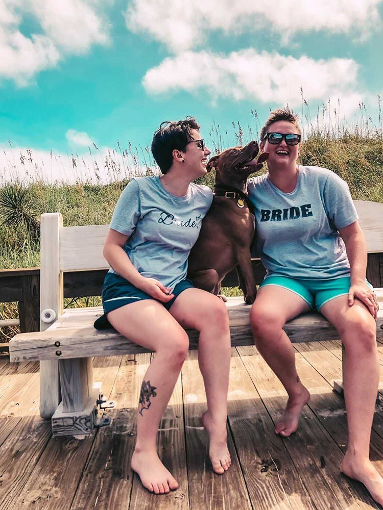 Two People Wearing Grey Bride Tees on a Bench at the Beach with a Dog